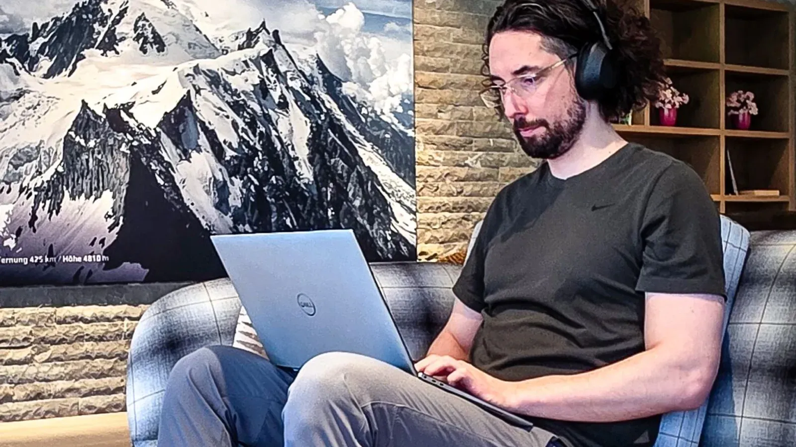 A developer working on a laptop in a wood-panelled chalet lounge with a Mont Blanc photograph on the wall — coding the Krypto Politik relaunch during a family holiday in the Allgäu.